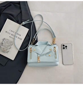 Detail of light blue motorcycle jacket style handbag with metal zippers and gold studs
