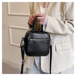 Close-up of black leather crossbody square bag with silver hardware on a beige blazer