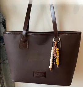 Detail of dark brown tote bag showing textured fabric and colorful bead charm accessory
