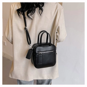 Detailed view of black leather crossbody square bag with front zipper pocket on model