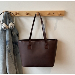 Detailed view of dark brown leather tote bag with long handles hanging on a wall hook