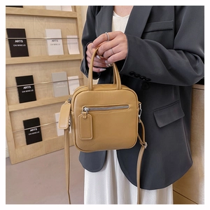 Detail of minimalist yellow square bag featuring smooth leather and silver hardware zipper