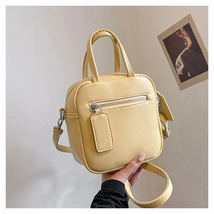 Detail view of a pale yellow crossbody bag with silver zippers and removable strap