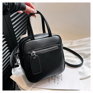 Detailed view of black square bag with smooth matte PU texture and front zipper pocket