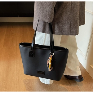 Detail of black faux leather tote bag with elegant beaded charm and brand logo patch