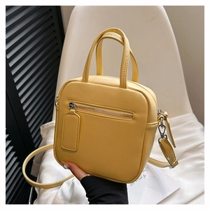 Detail of a yellow square crossbody bag with front zipper and top handle detail