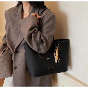 Black leather tote bag with colorful beaded charm detail shown on a brown tweed blazer