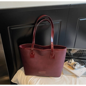 Close-up of deep red saffiano leather tote bag with logo plate and office desk accessories