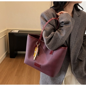 Detail of burgundy leather tote bag with colorful wooden beads on grey tweed blazer