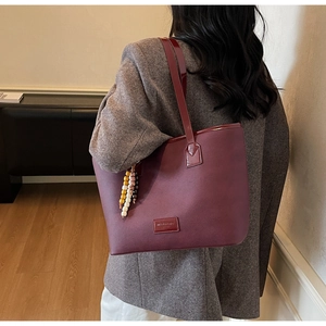 Detail of burgundy large tote bag with elegant beaded pendant and glossy handles