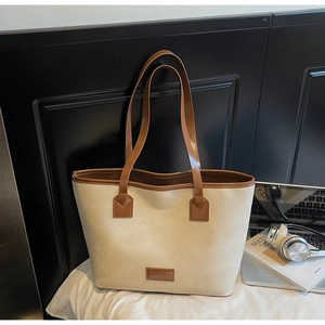 Detail of beige tote bag with dark brown leather straps and branded patch on white surface