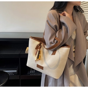 Detail view of cream canvas tote bag with brown leather trim and beaded tassel pendant