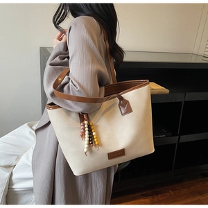 Detail of canvas tote bag with brown leather trim and colorful beaded tassel charm