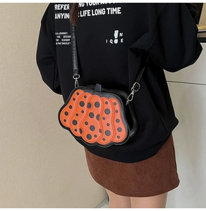 Borsa a tracolla a forma di zucca con pois neri mostrata in dettaglio laterale alla moda