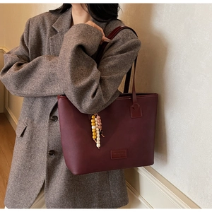 Detail of burgundy leather tote bag with colorful beaded charm on grey wool blazer