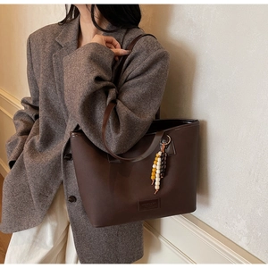 Detail of dark brown leather tote bag with unique beaded pendant and minimalist logo patch