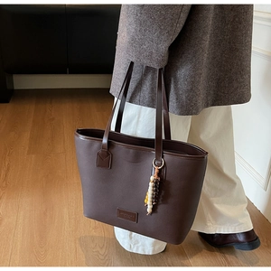 Detail of deep brown tote bag with cross-grain texture and colorful beaded tassel charm