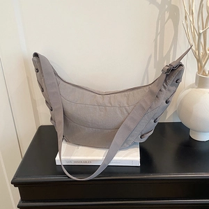 Light grey hobo shoulder bag with quilted texture and side lace-up details on a black cabinet