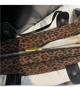 Detailed close-up of the smooth golden metal zipper and black leather handle on leopard tote