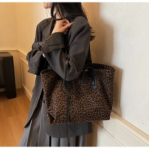 Detail view of a large leopard print tote bag with black leather straps on a model in a suit