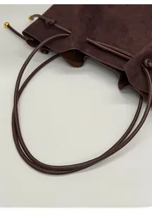 Detail of dark brown suede tote bag featuring slender straps and gold metal ball accents