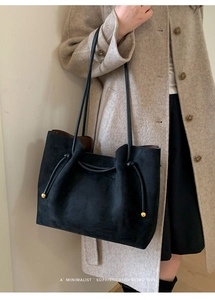 Detailed close-up of a black suede tote bag with drawstring and gold bead hardware detail