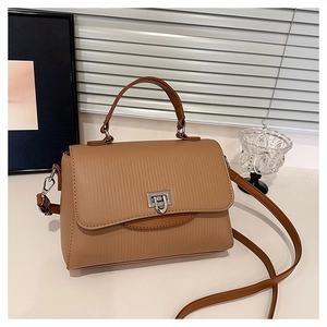 Detail of tan handbag featuring vertical striped texture and silver square turn-lock closure