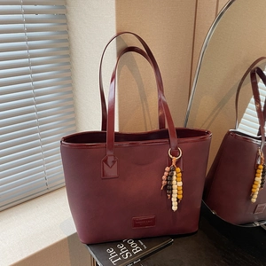 Burgundy vintage leather tote bag with beaded tassel in a stylish indoor setting