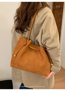 Detail of a brown suede tote bag with drawstring closure and golden spherical metal hardware