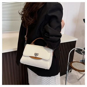 Detail of cream crossbody bag with brown handles and silver twist lock on a model