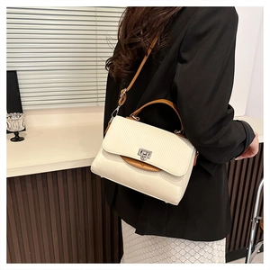 Detail of cream striped handbag with brown trim and silver metal buckle on black blazer