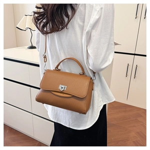Detail of tan striped handbag with silver buckle worn by model in a minimalist home setting