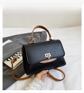 Detail of black pebbled crossbody bag with brown handle and metal square clasp closure