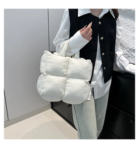 Close-up of a white quilted puffer tote bag with soft texture held by a model