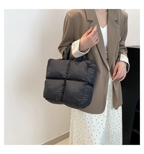 Model holding a black quilted puffer tote bag, showing its soft texture and medium size