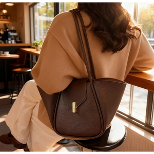 Detail of dark brown leather tote bag with gold buckle on shoulder of woman in wool coat