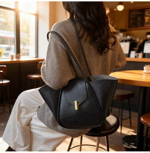 Close-up of black retro textured leather tote bag with golden metal clasp and wing design