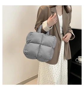 Quilted puffer tote bag in grey-blue nylon fabric shown held by a model in a minimal setting