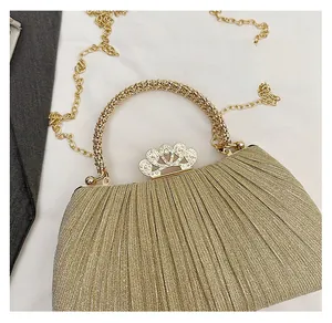 Detail of evening bag with golden pleated fabric, crown rhinestone clasp and beaded handle