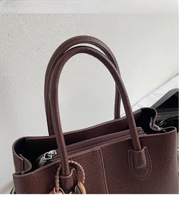 Detail of deep brown tote bag showing litchi grain texture and metal zipper closure