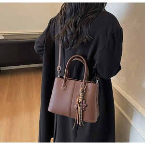 Detailed view of dark brown pebbled leather tote bag with decorative tassel on a model