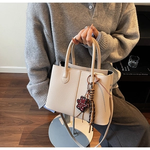Close-up of creamy white lychee-pattern leather tote bag with stylish bicolor pendant