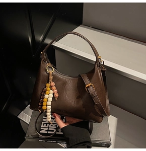 Détail du sac en cuir marron foncé avec breloque perlée et logo gaufré sur le côté