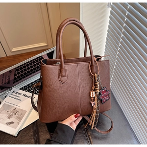 Detail of dark brown pebble leather tote bag with heart bear charm on a desk