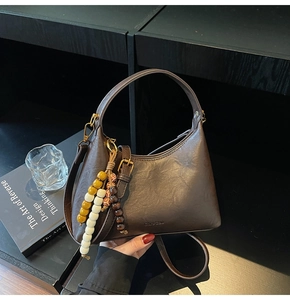 Gros plan détaillé d'un sac hobo marron avec breloque en perles et logo embossé