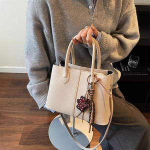 Detail of beige lychee grain leather tote bag with red leopard bear charm and woven cord