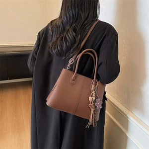 Brown tote bag with leopard bear charm and tassel detail worn over a black blazer