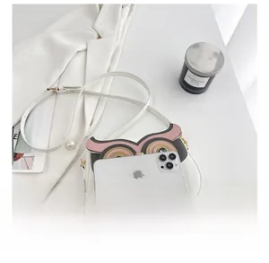 Détail du sac hibou avec patchwork en cuir et yeux en strass à côté d'un smartphone