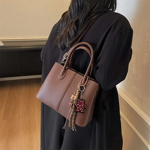 Brown litchi grain leather tote bag with bear charm and tassel on a model in a black coat