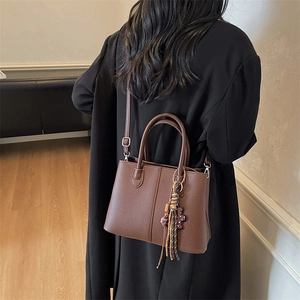 Detail of brown litchi pattern tote bag with tassel and bear charm accessories